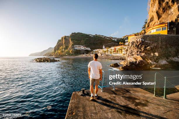 rear view of a man looking at sunset in the ocean from ponta do sol town, madeira island, portugal - explorador imagens e fotografias de stock