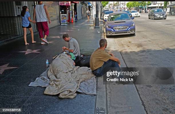 Los Angeles, CA People who are displaced sit on the sidewalk with two dogs on Hollywood Blvd on August 12, 2023 in Los Angeles, CA.