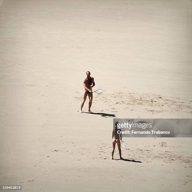 Pareja jugando al tenis en la playa pacticando el nudismo