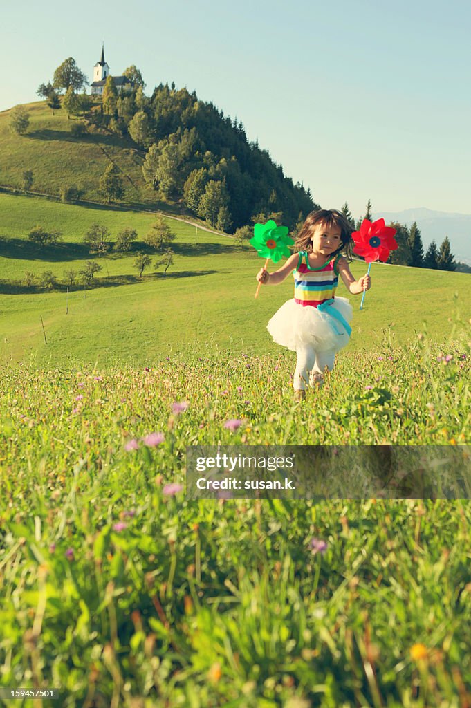 Girl holding toy windmill running happily on hill