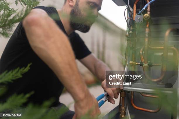 un technicien concentré installe une pompe à chaleur extrêmement respectueuse de l’environnement - remplacement photos et images de collection