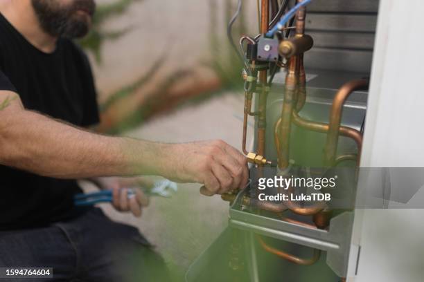 an unrecognizable man installs a heat pump in the courtyard of a residential building - heating home stock pictures, royalty-free photos & images
