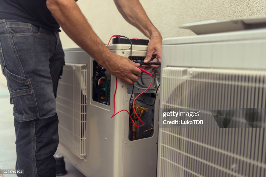 An unrecognizable electrician installs a heat pump in the courtyard of a residential building