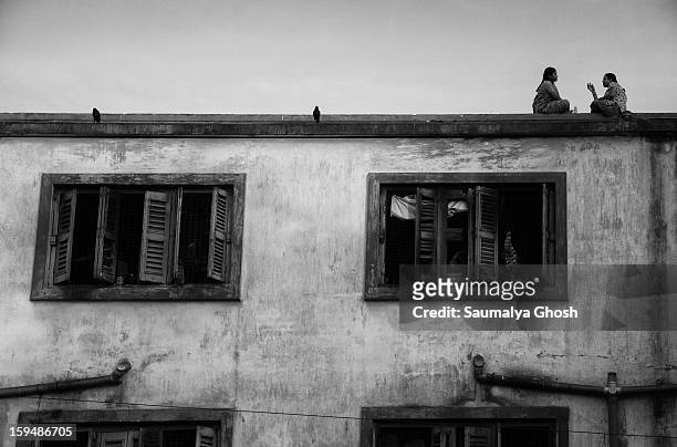 In a beautiful afternoon, two women, sitting on the edge of a rooftop, are busy in chit chat.