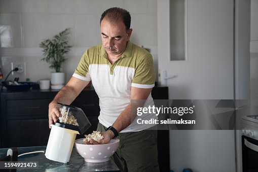 Photo of mature adult man using hot air popcorn maker for cooking popcorns Photo of mature adult man using hot air popcorn maker for cooking popcorns