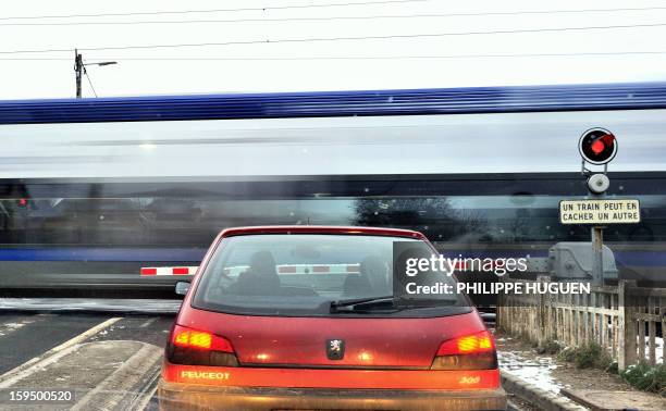 Car waits as a regional train passes at a level crossing in Fletre, northern France, on January 14, 2013. AFP PHOTO / PHILIPPE HUGUEN