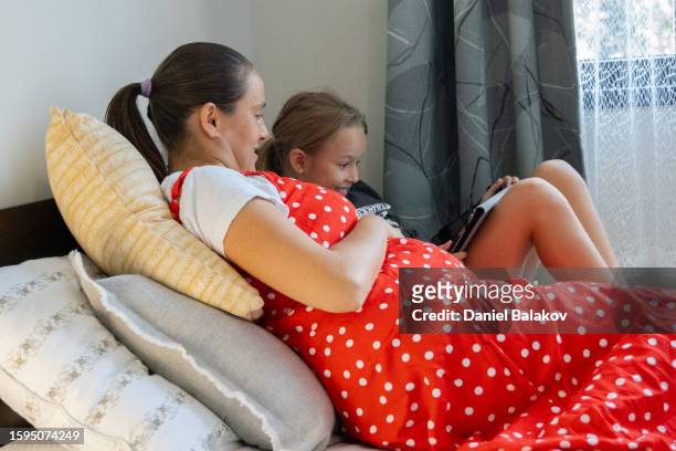 mom and daughter binge-watch tv series on the bed. - binge tv stockfoto's en -beelden