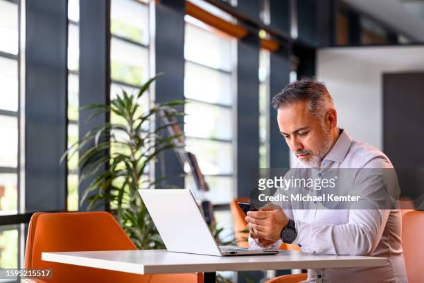 portrait of a mature businessman with laptop looking at his mobile phone - kind computer stock pictures, royalty-free photos & images