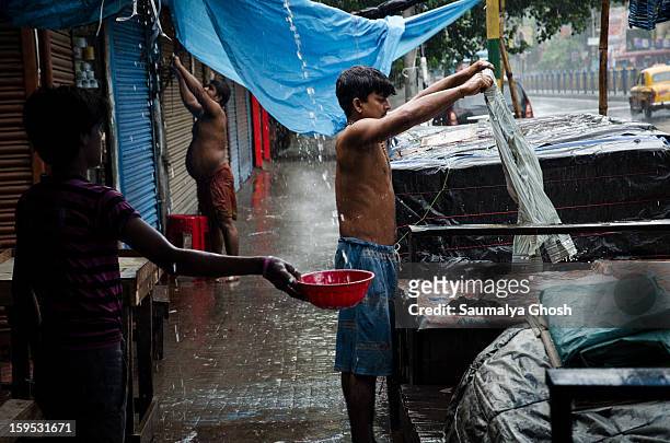 Kolkata street scene in a rainy day. A dhobi is washing clothes and a boy is collecting water in a pot.