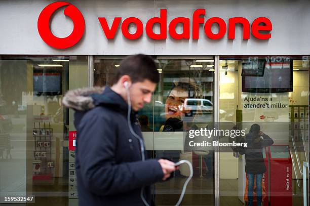 Pedestrian wearing headphones looks at his mobile phone as he passes the front of a Vodafone Group Plc store in Barcelona, Spain, on Tuesday, Jan....