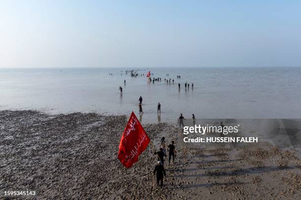 Shiite Muslim pilgrims wave flags as they walk in the Gulf waters and a muddy shore, at the start of their march from Iraq's southern city of al-Faw...