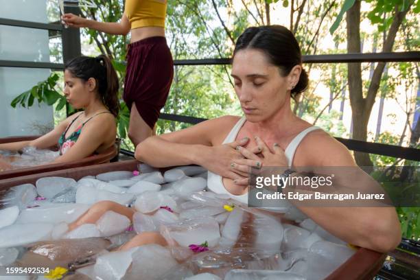 two women take an ice bath or cryotherapy on a terrace with trees in the background - ice bath stock pictures, royalty-free photos & images