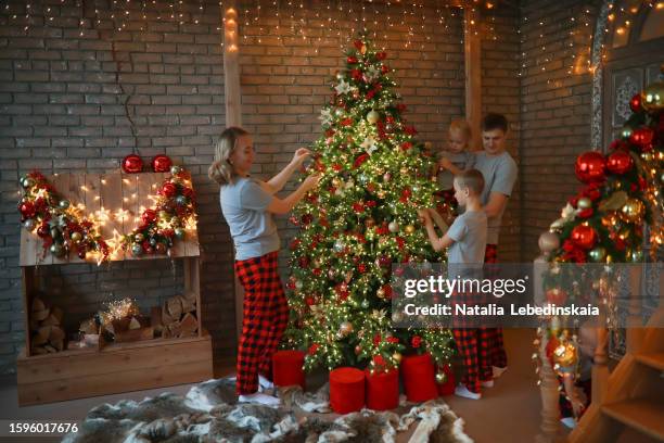 cozy christmas tree decorating: large family with three children and toddler in identical pajamas. - decorating-the-christmas-tree stock pictures, royalty-free photos & images