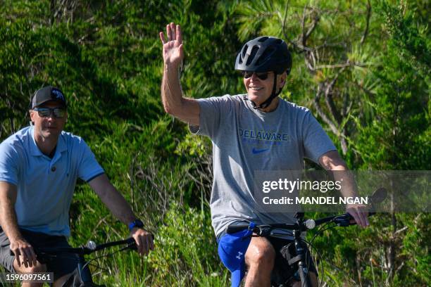 President Joe Biden waves as he rides his bicycle through Gordons Pond in Cape Henlopen State Park in Rehoboth Beach, Delaware on August 13, 2023.