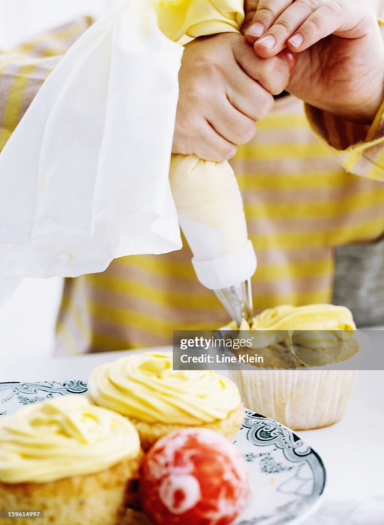 Hands icing cupcake on table