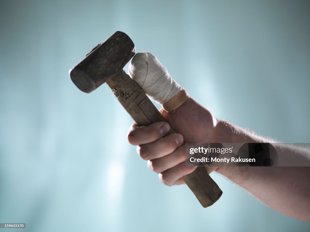 Man with bandaged thumb holding hammer