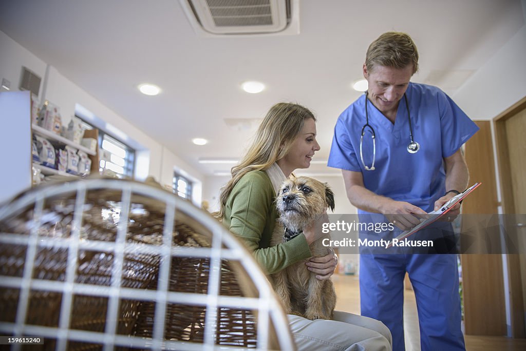 Vet talking to woman holding pet dog in veterinary waiting room