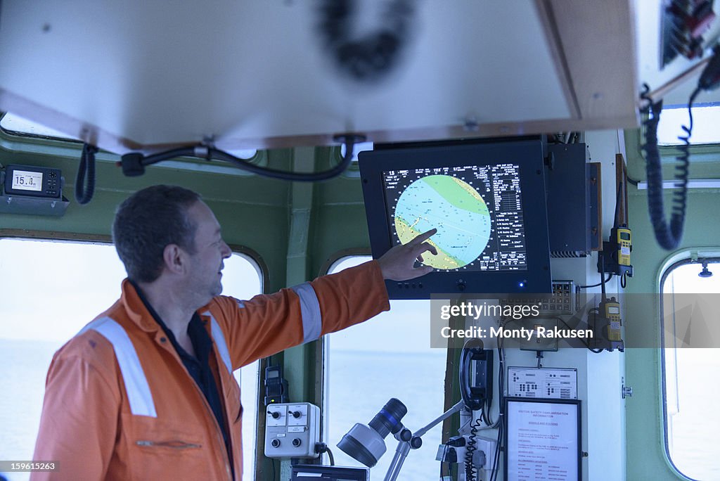 Ships mate pointing at digital chart on monitor on tug