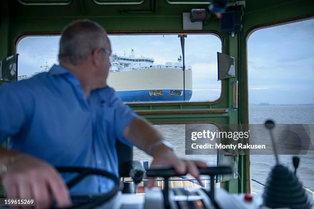 tug captain steering tug, looking over shoulder to ship at sea - skipper stockfoto's en -beelden