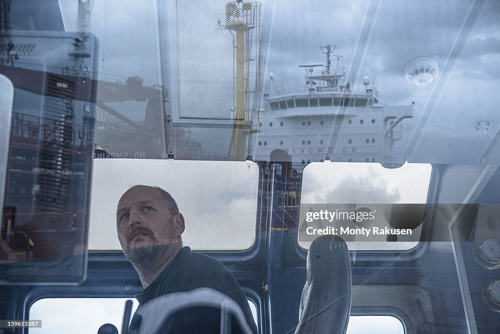 Tug captain looking into distance, with reflections of ship on glass
