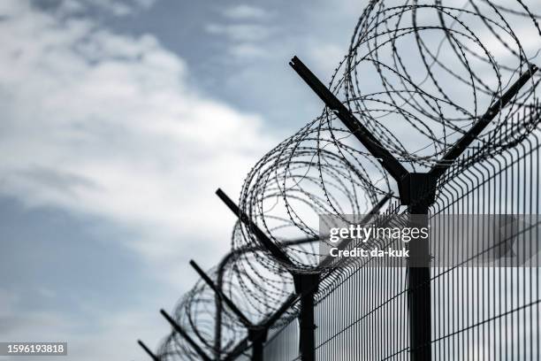 barbed wire fence. jail or border fence with razor wire against dark sky. security concept - escaping jail stock pictures, royalty-free photos & images