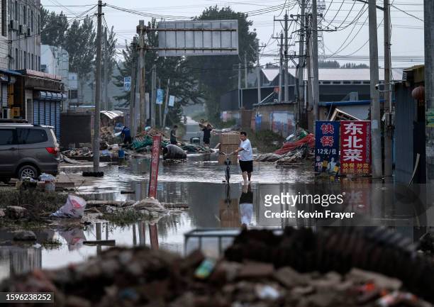 Man carries boxes of goods salvaged from a local business on a bicycle as he wades through receding floodwaters on August 5, 2023 in Zhuozhou, Hebei...