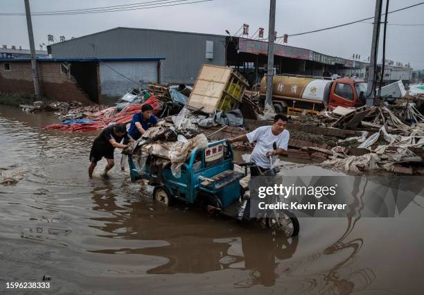 People push a three wheeler with salvaged goods from a local business through receding floodwaters on August 5, 2023 in Zhuozhou, Hebei Province...