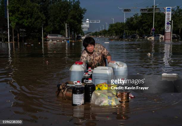 Woman pushes a makeshift raft full of goods salvaged from a building as she wades through receding floodwaters on August 5, 2023 in Zhuozhou, Hebei...