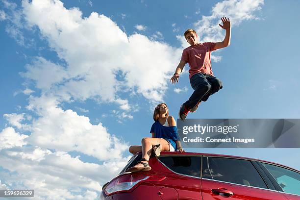 young man jumping off car roof, girl sitting on roof - ego perspektive stock-fotos und bilder