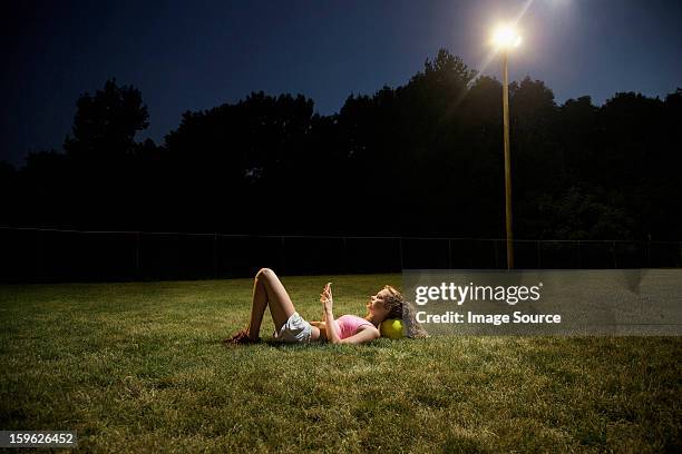 girl using cell phone lying on soccer pitch at night - football phone stock pictures, royalty-free photos & images