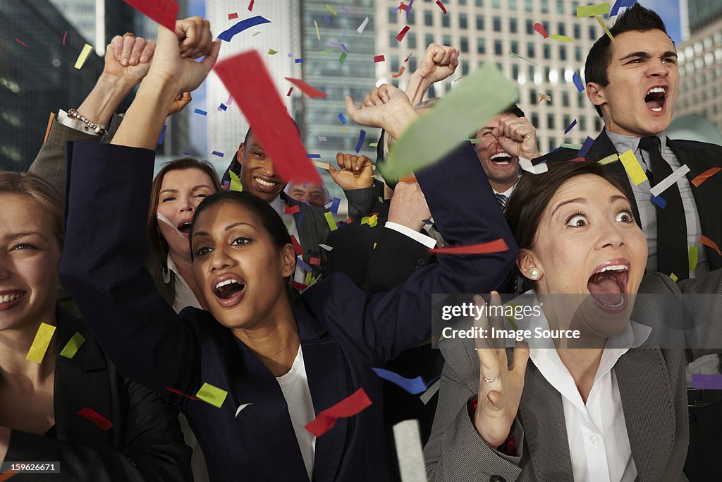 Businesspeople cheering as ticker tape falls