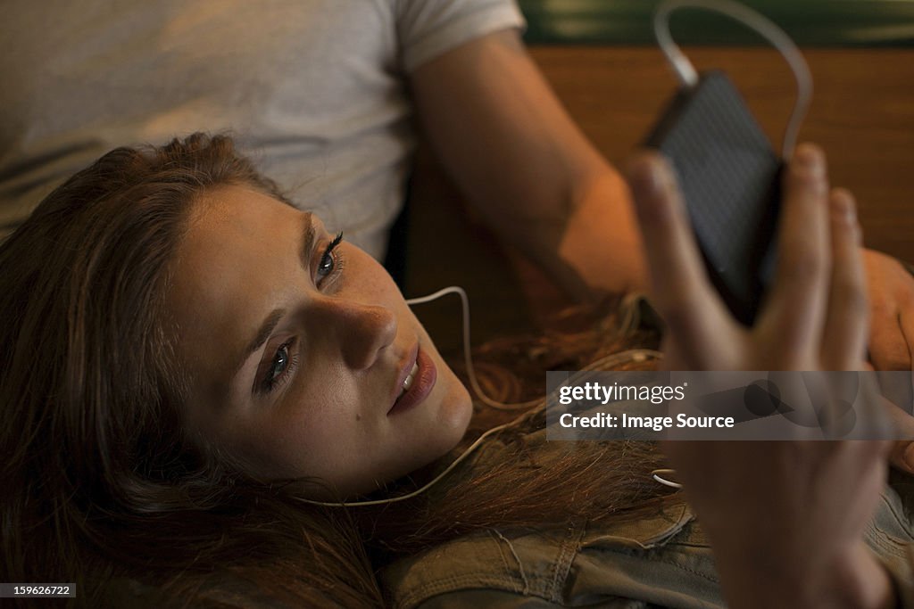 Young woman listening to music, lying on boyfriend's lap