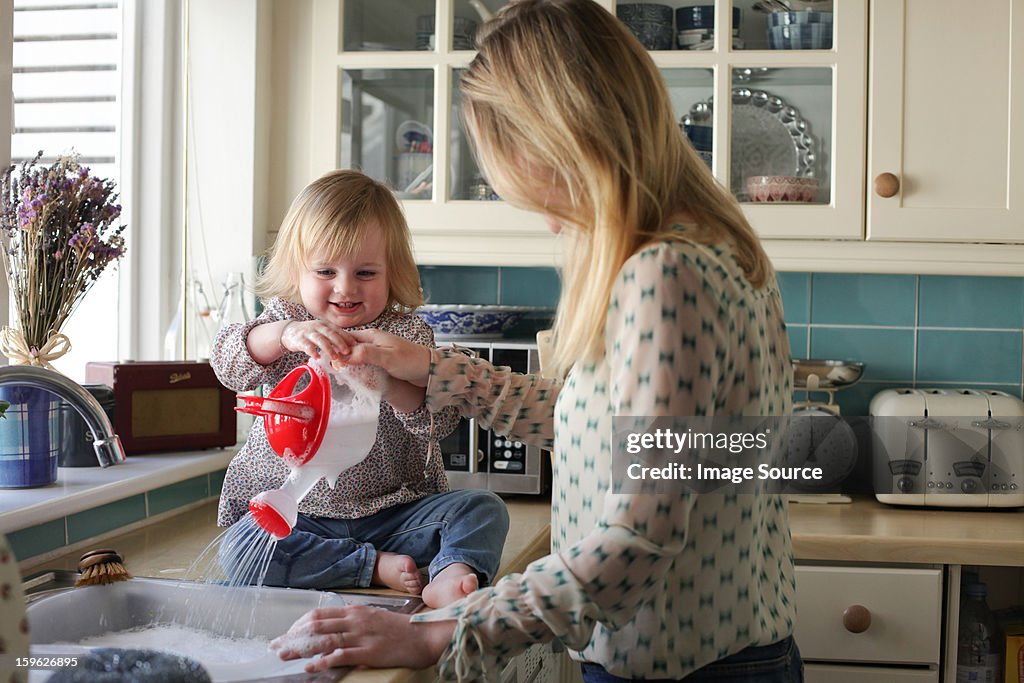 Mother washing up, daughter pouring water