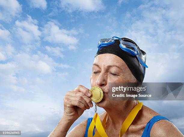 senior woman wearing swimming cap kissing gold medal - médaillé photos et images de collection