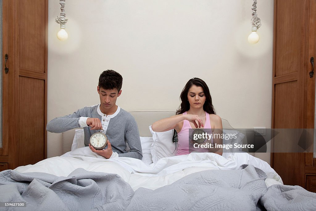 Couple in bed setting alarm clocks