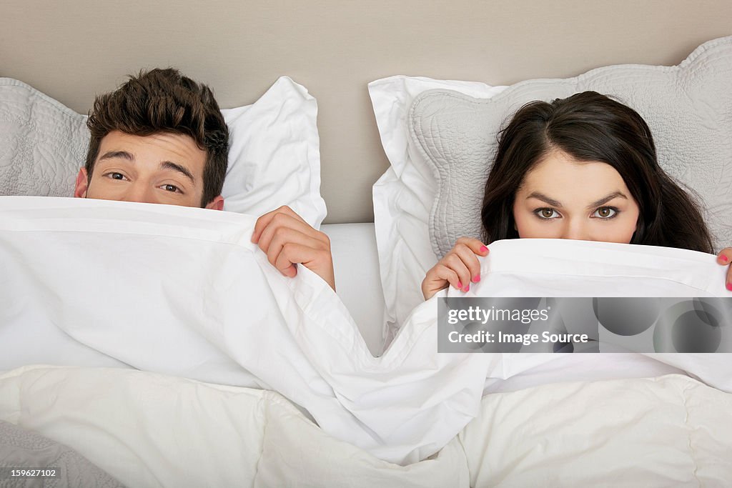 Couple in bed peeking behind duvet