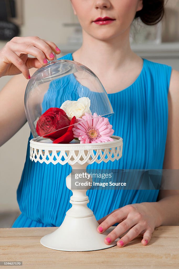 Woman lifting lid of cake stand with flowers