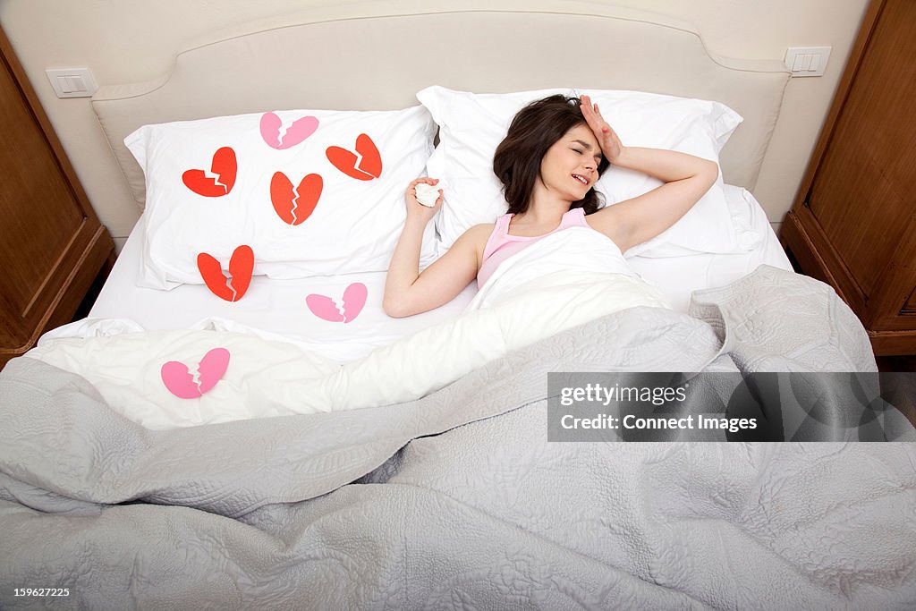 Woman crying in bed with broken heart shapes on bedclothes
