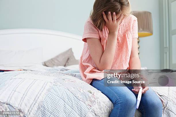 teenage girl sitting on bed with pregnancy test - tienerzwangerschap stockfoto's en -beelden