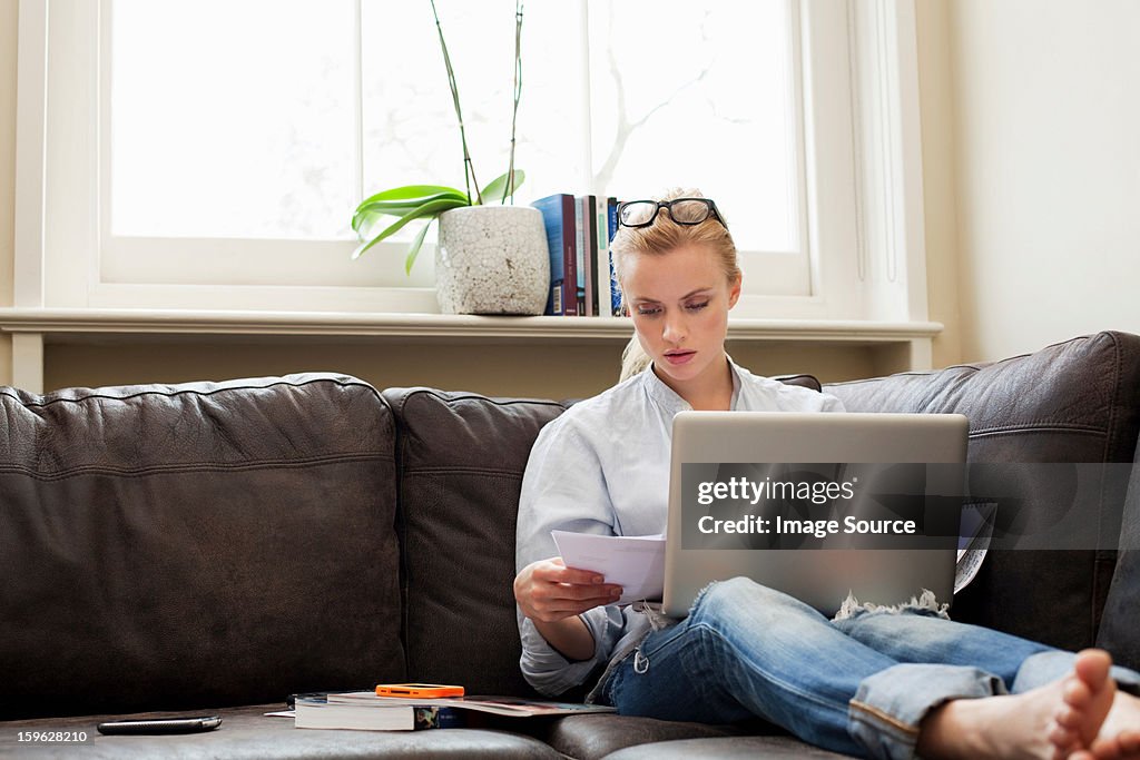 Young woman sitting on sofa with laptop and papers