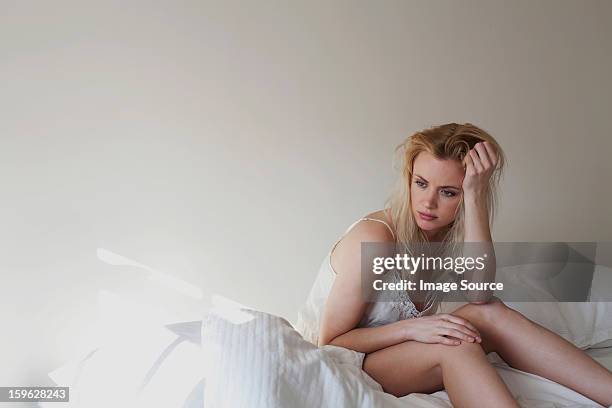 upset young woman sitting on bed - temi legati alla sessualità foto e immagini stock