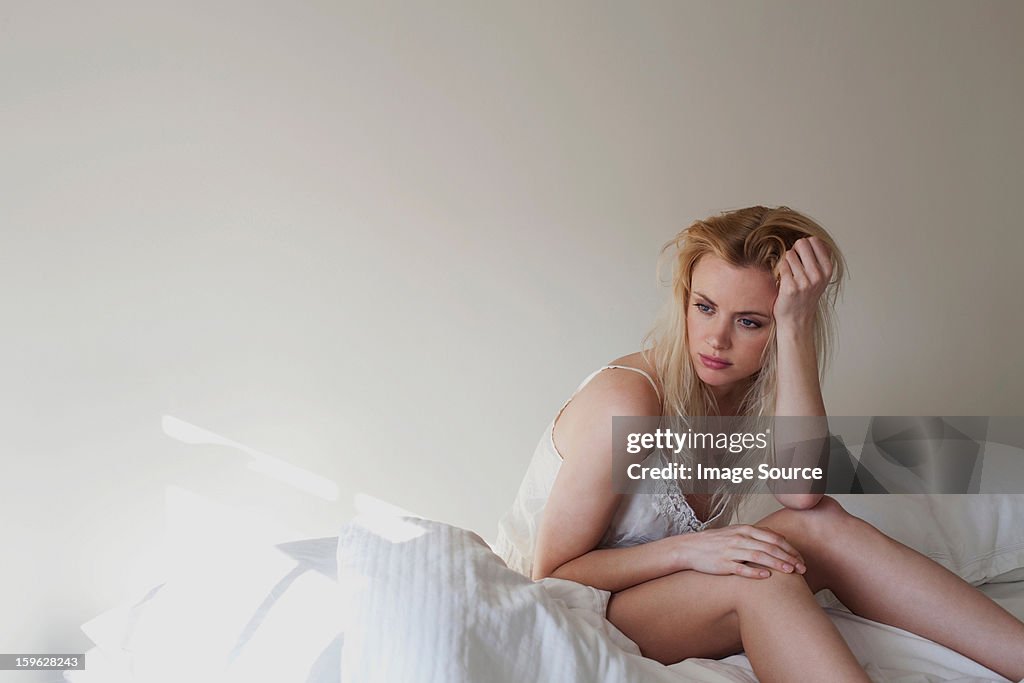 Upset young woman sitting on bed