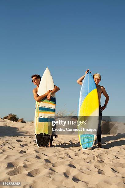 two young men standing behind surfboards on beach - portugal beach stock pictures, royalty-free photos & images