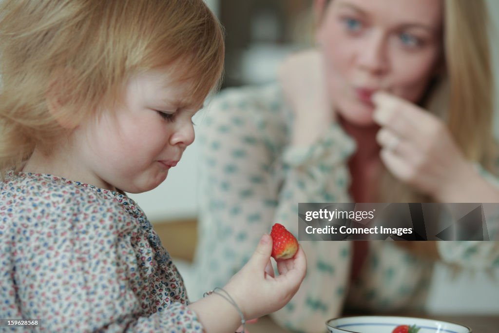 Toddler holding strawberry, pulling face