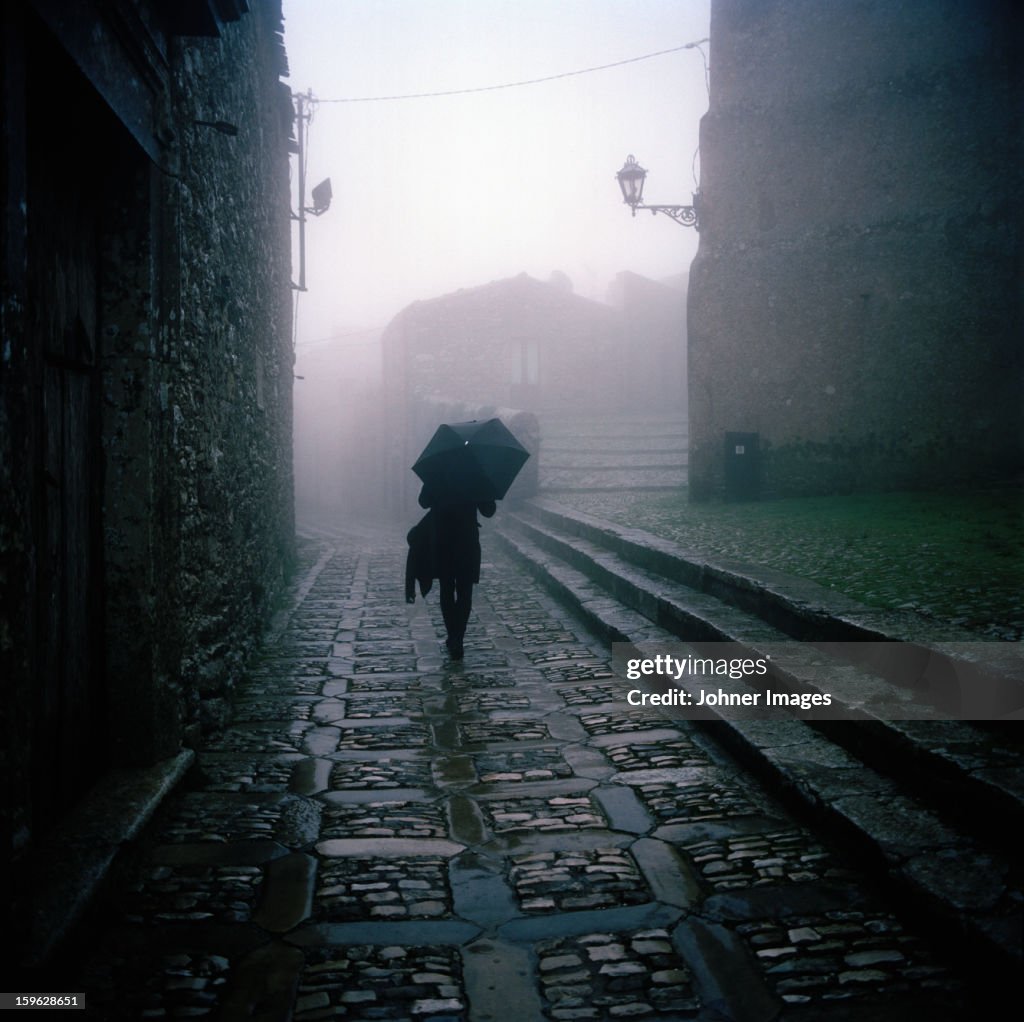 A woman with an umbrella walking on a street, Italy.