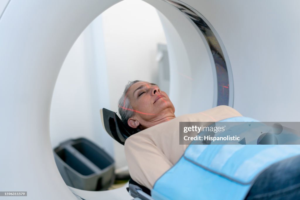 Mature woman lying down on a CAT scan machine with eyes closed at the hospital