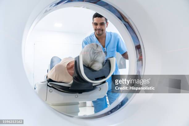 cheerful male technician adjusting the machine before starting the cat scan of an unrecognizable senior woman lying down on machine - radiologist stock pictures, royalty-free photos & images