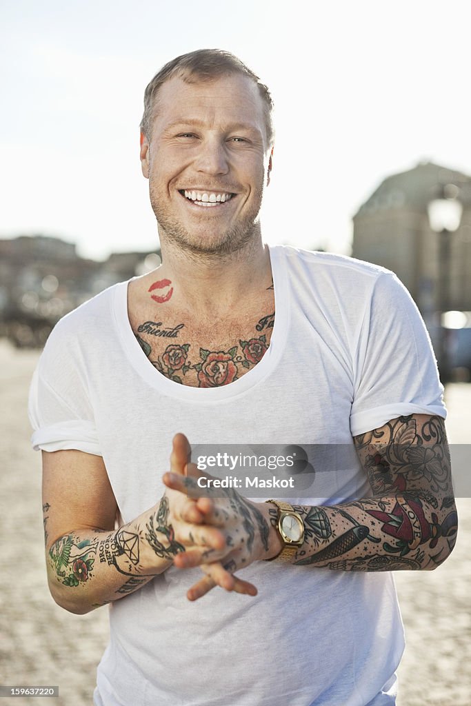 Portrait of a happy tattooed man standing with hands clasped
