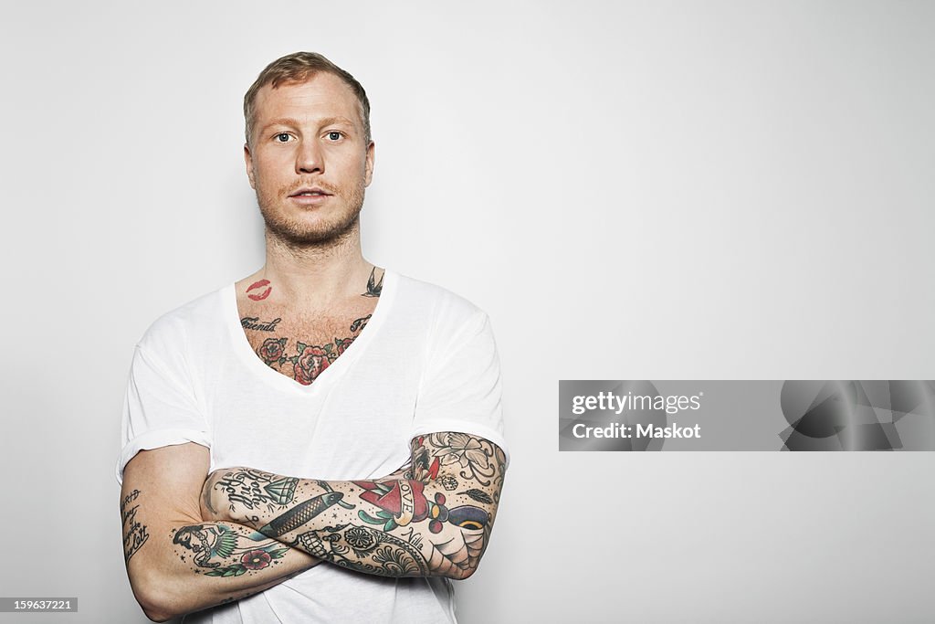 Portrait of a tattooed man with arms crossed standing against grey background