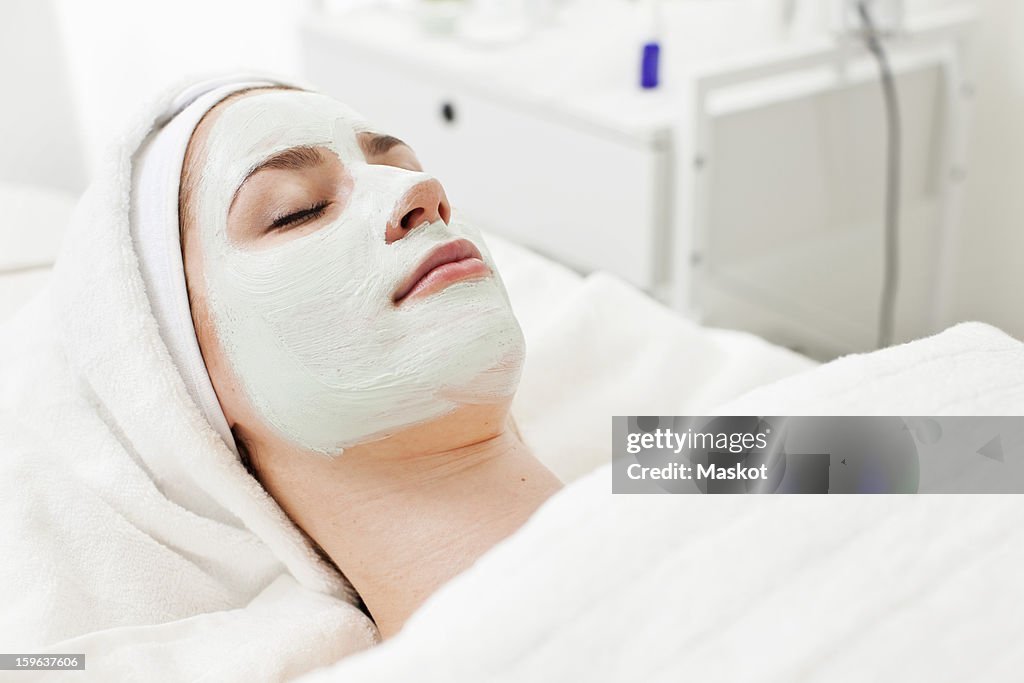 Young woman relaxing on massage table with facial mask at beauty spa